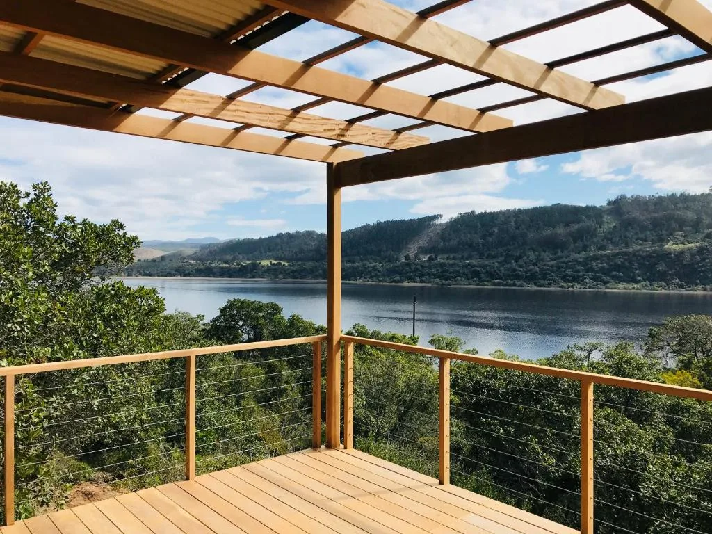 Wooden deck with pergola overlooking serene lagoon and forested hills