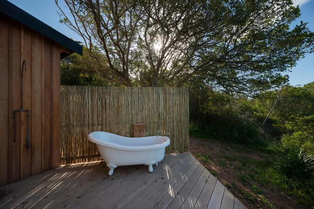 Outdoor freestanding bathtub on wooden deck with natural screening and trees