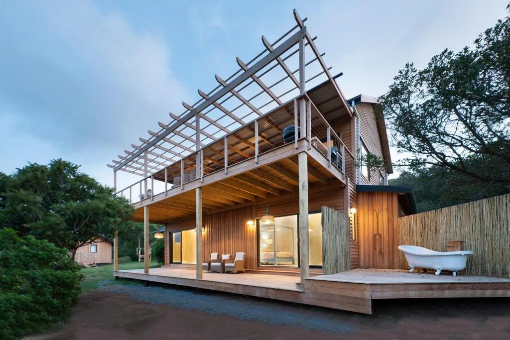 Modern wooden cabin with pergola deck and outdoor bathtub at dusk