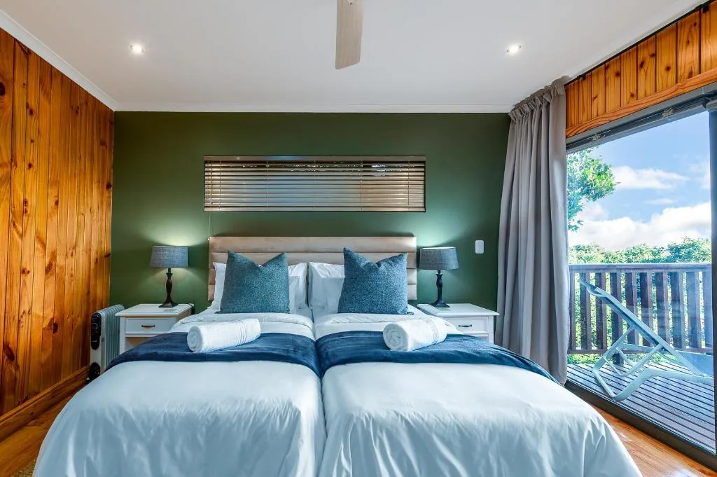 Modern bedroom with twin beds, green accent wall, wooden paneling, and deck access