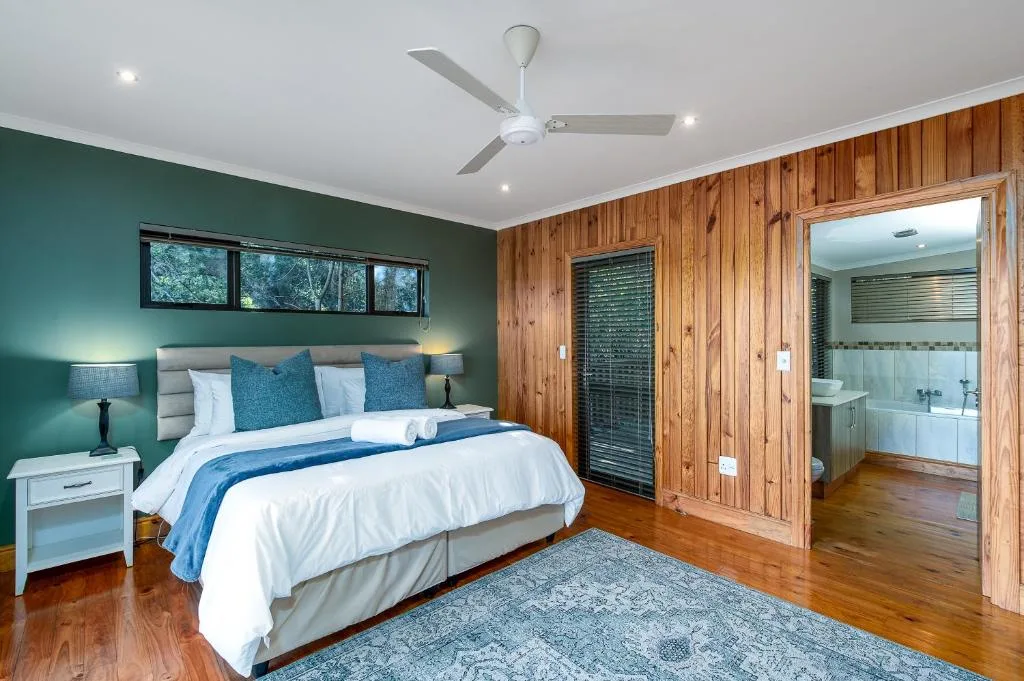Spacious bedroom with teal accent wall, wooden paneling, and ensuite bathroom access