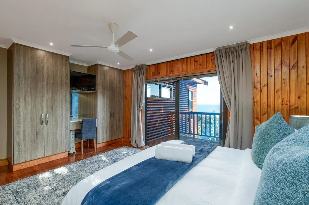 Spacious bedroom with ocean view deck, wooden paneling, and modern furnishings