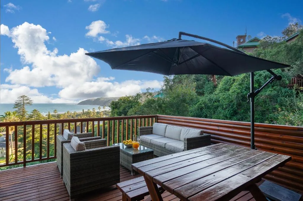 Spacious wooden deck with ocean views, lounge seating, dining table, and umbrella