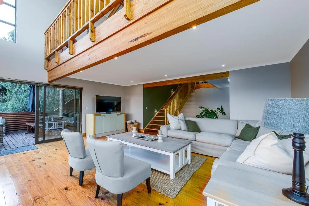 Modern open-plan lounge with grey sofa, accent chairs, wooden beams, and stairs