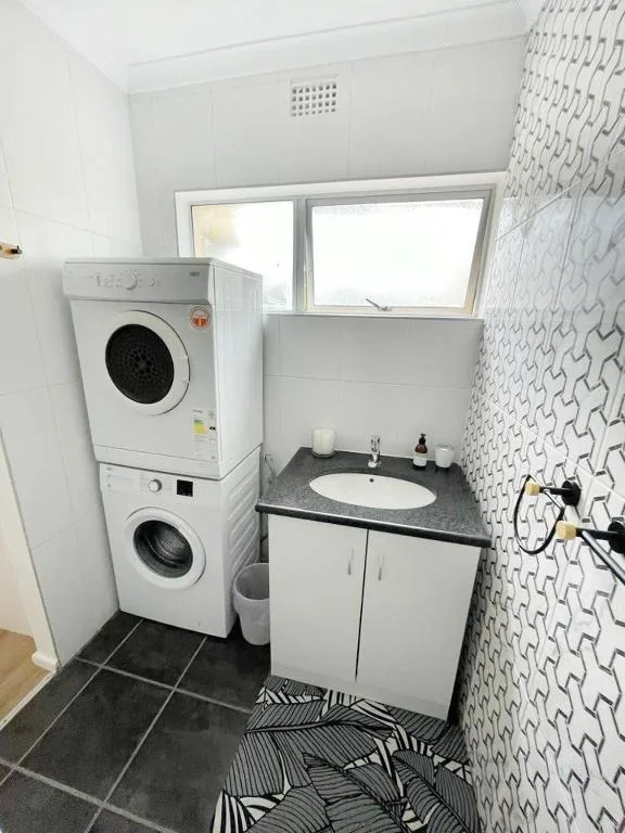 Modern bathroom with stacked washer and dryer, round sink, and patterned wall tiles