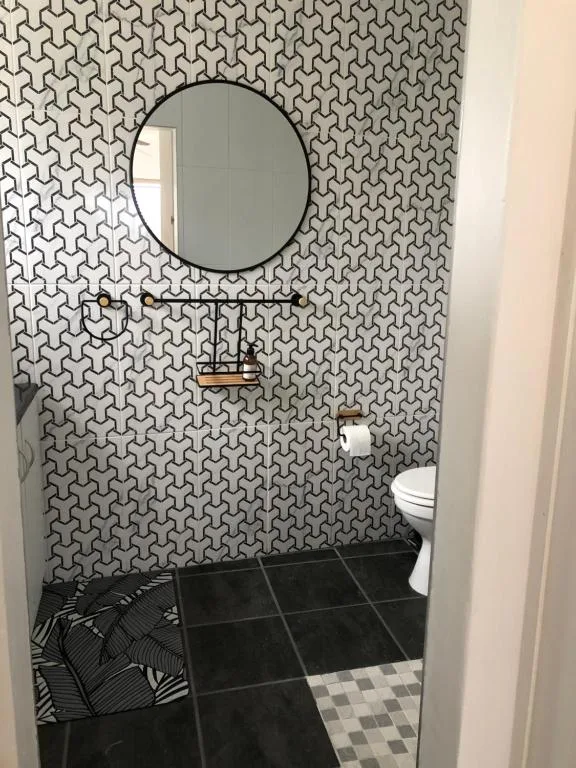 Modern bathroom with geometric patterned wallpaper, round mirror, and black tile flooring