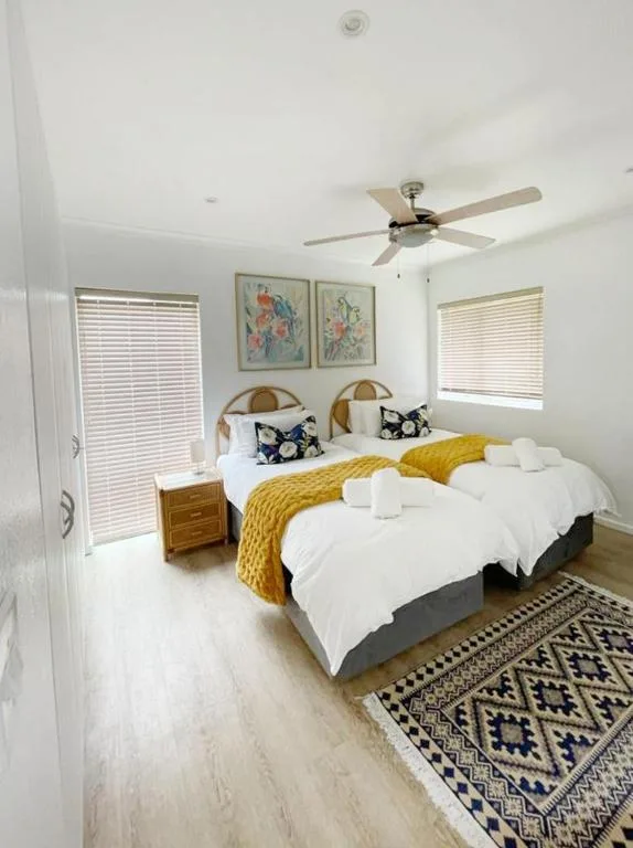 Bright bedroom with twin beds, yellow throw, woven headboards, ceiling fan