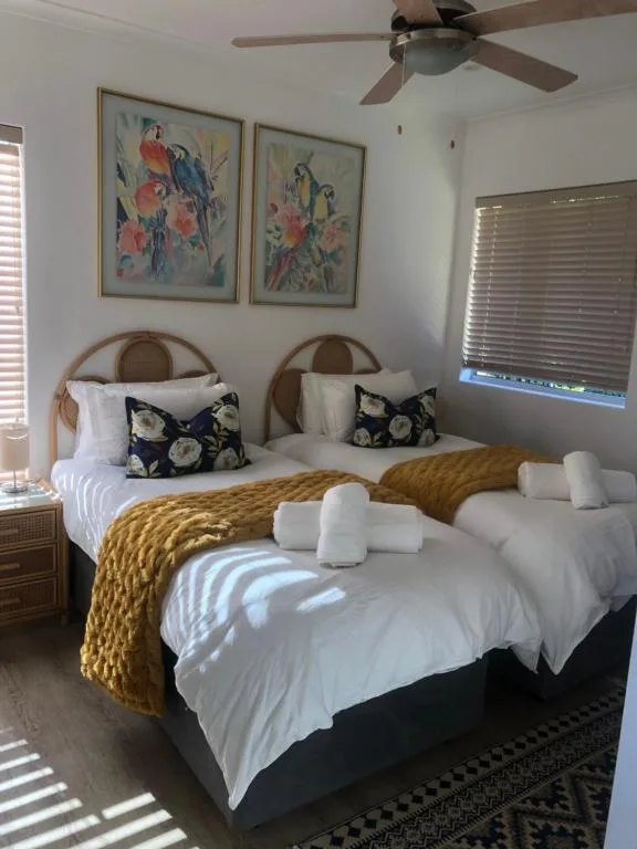 Bright bedroom with two twin beds, colorful parrot artwork, and ceiling fan