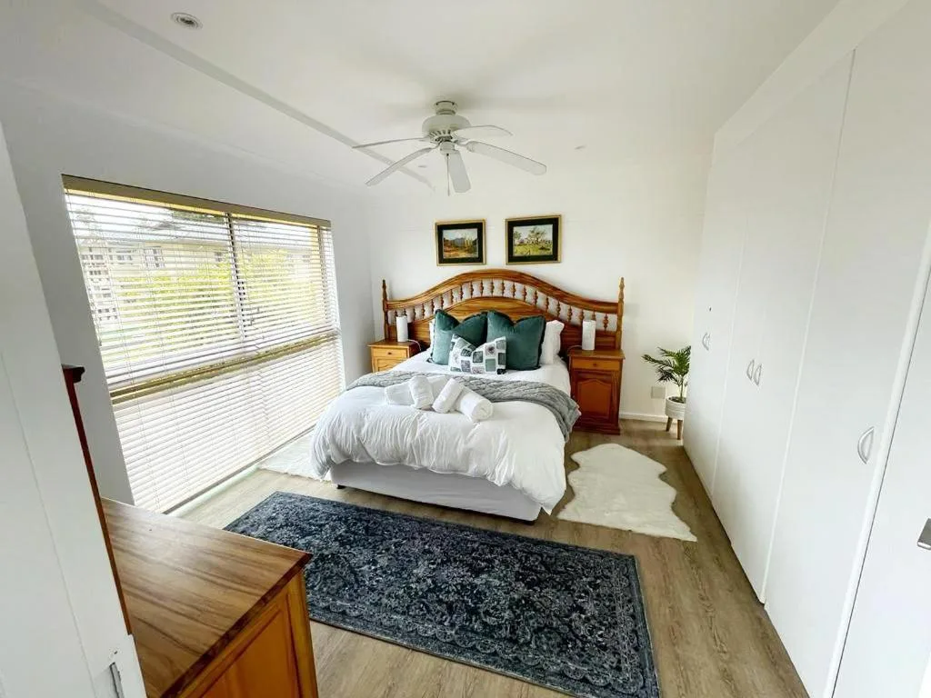 Bright bedroom with wooden bed frame, white bedding, and ceiling fan