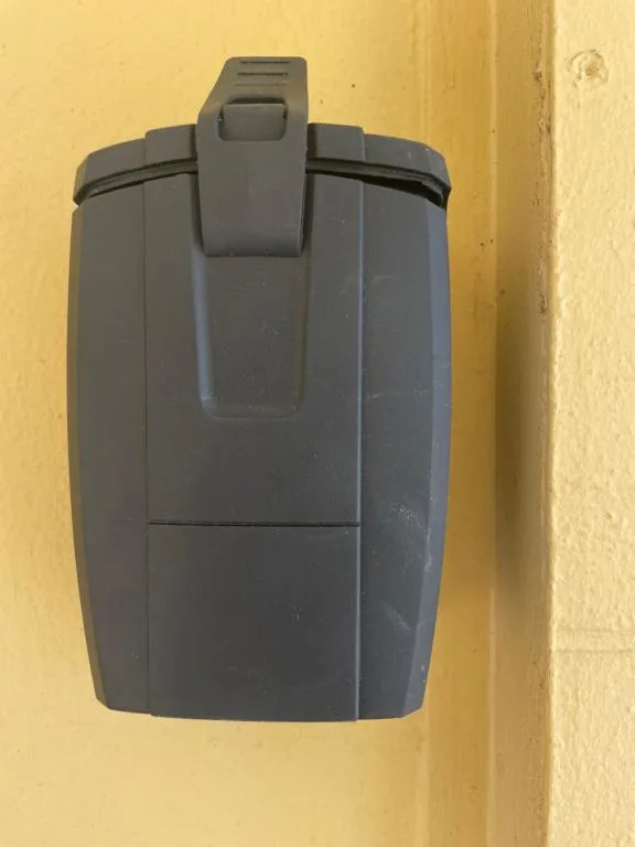 Black electrical outlet box mounted on yellow exterior wall