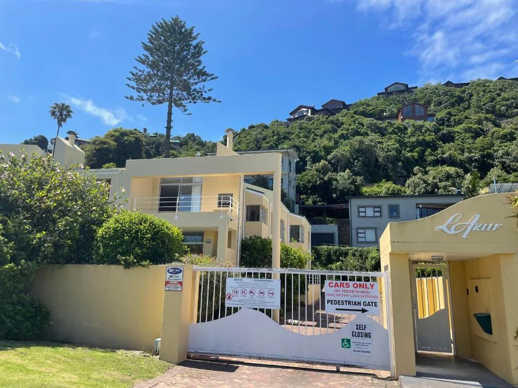 Modern cream-colored apartment building with gated entrance and lush hillside vegetation