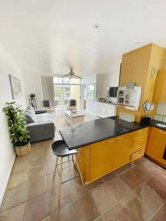 Modern kitchen with yellow cabinetry and black countertop island overlooking open-plan lounge