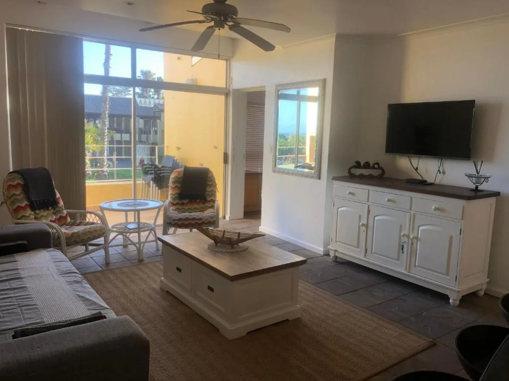 Bright lounge with sofa, TV, ceiling fan, and ocean views through glass doors