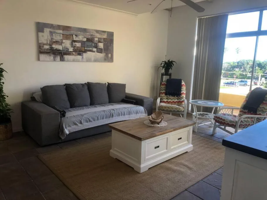 Modern lounge with dark sofa, wooden coffee table, and large windows overlooking pool area