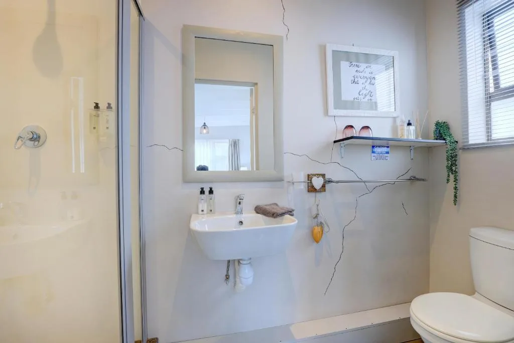 Bright bathroom with white basin, mirror, toilet, and coastal view through window