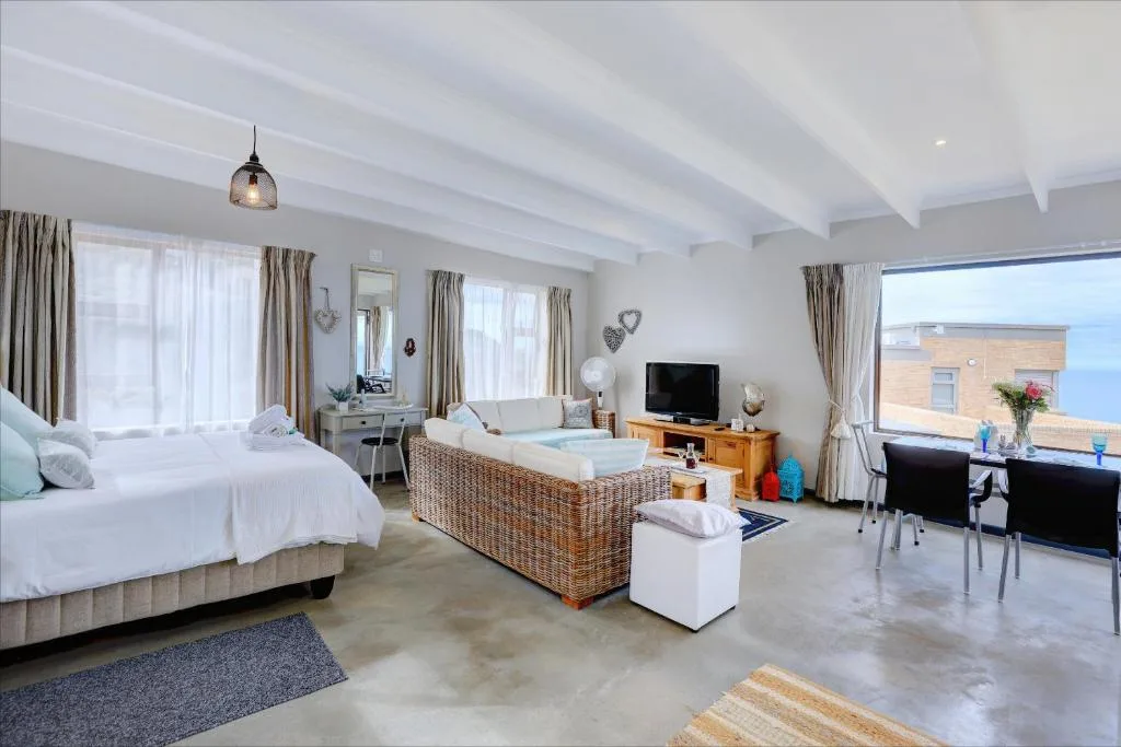 Spacious bright bedroom with bed, lounge area, and ocean views through windows