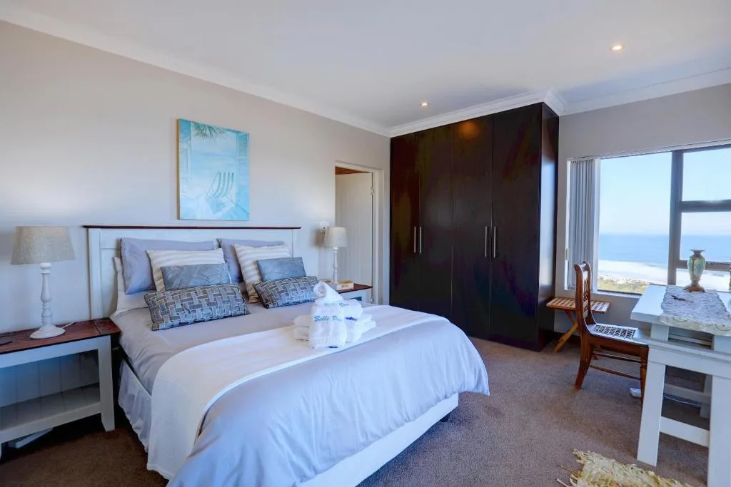 Bright bedroom with queen bed, ocean view windows, and dark wooden wardrobes