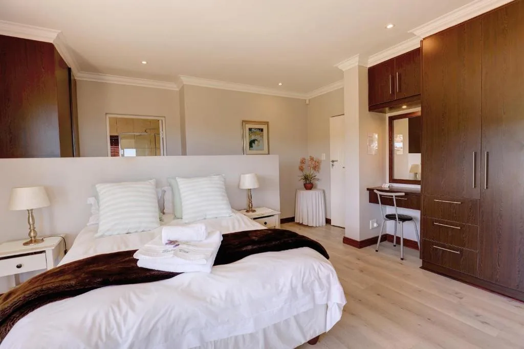 Spacious bedroom with white bedding, wood furnishings, and modern amenities