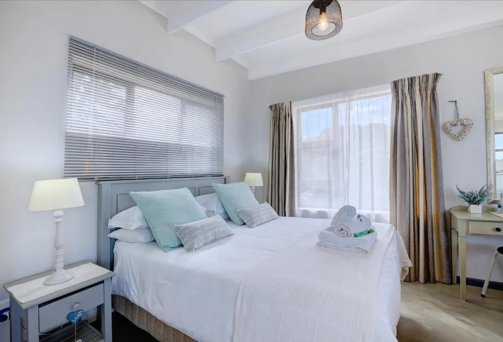 Bright bedroom with queen bed, turquoise pillows, bedside lamp, and garden views