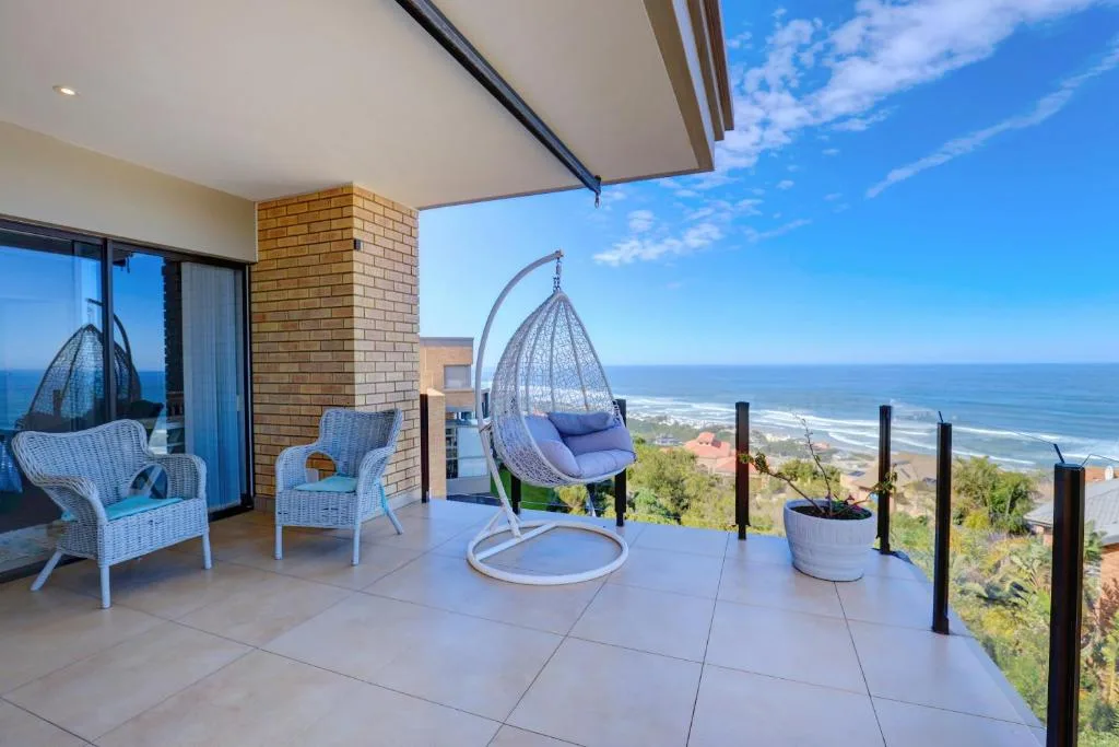 Spacious oceanview deck with hanging chair and wicker seating overlooking coastline