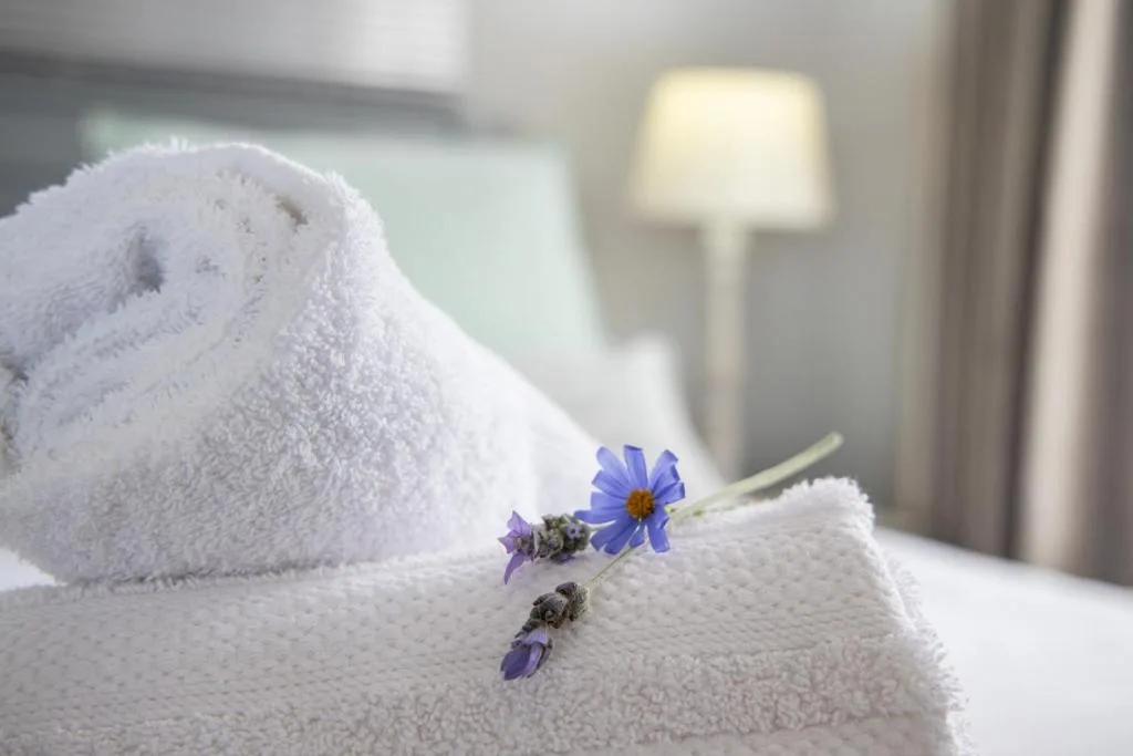 Rolled white towels with blue flower accent in bedroom setting