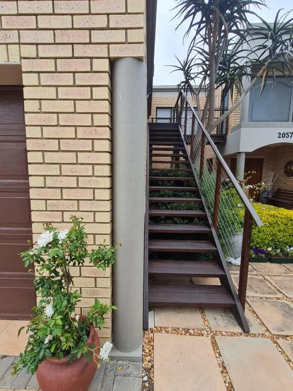 Brick building entrance with wooden stairs, metal railings, and potted plants