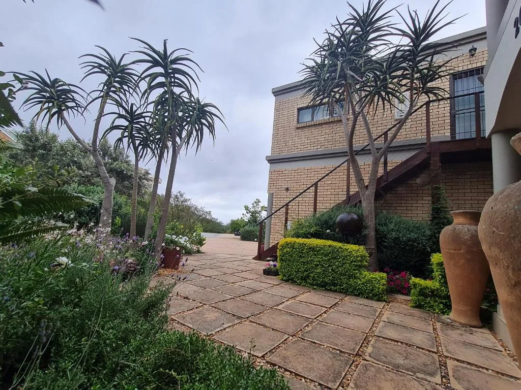 Brick home with manicured garden, palm trees, and paved courtyard entrance