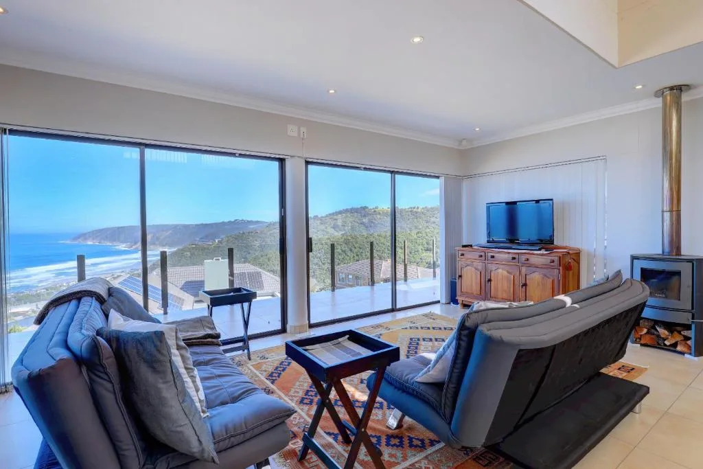 Spacious lounge with sofas, TV, and panoramic ocean and mountain views through glass doors