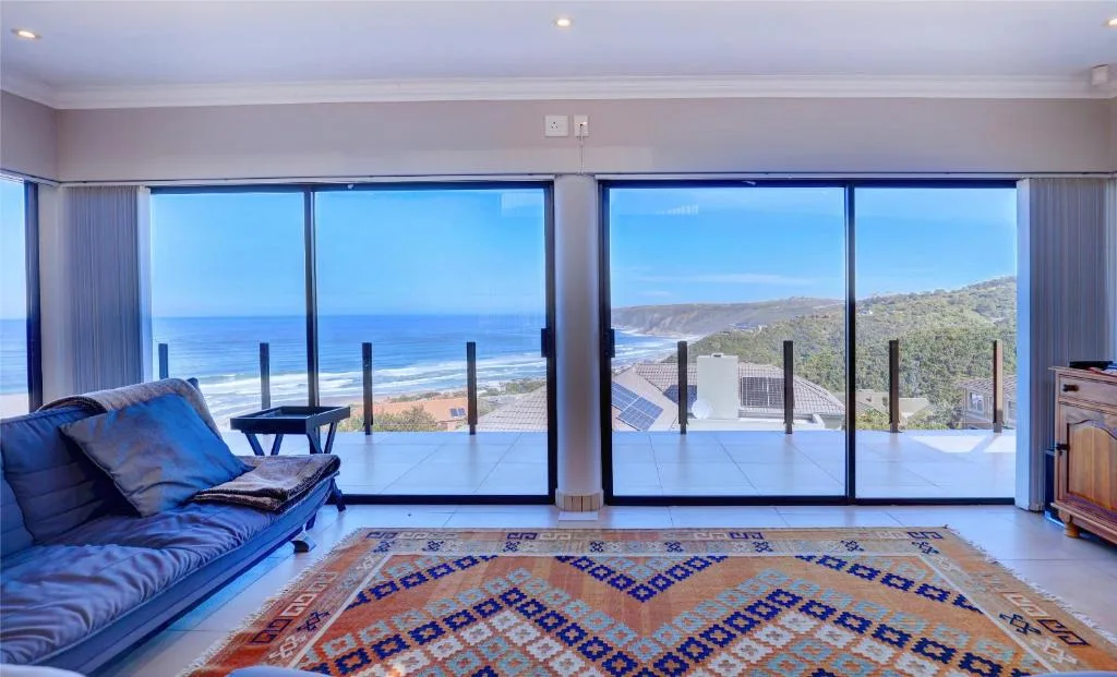 Expansive ocean and coastal mountain views from modern lounge with glass doors