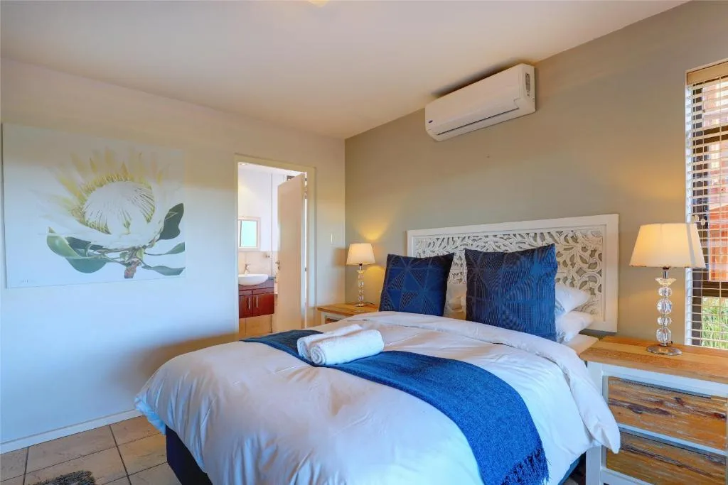 Bright bedroom with queen bed, blue pillows, botanical artwork, air conditioning unit