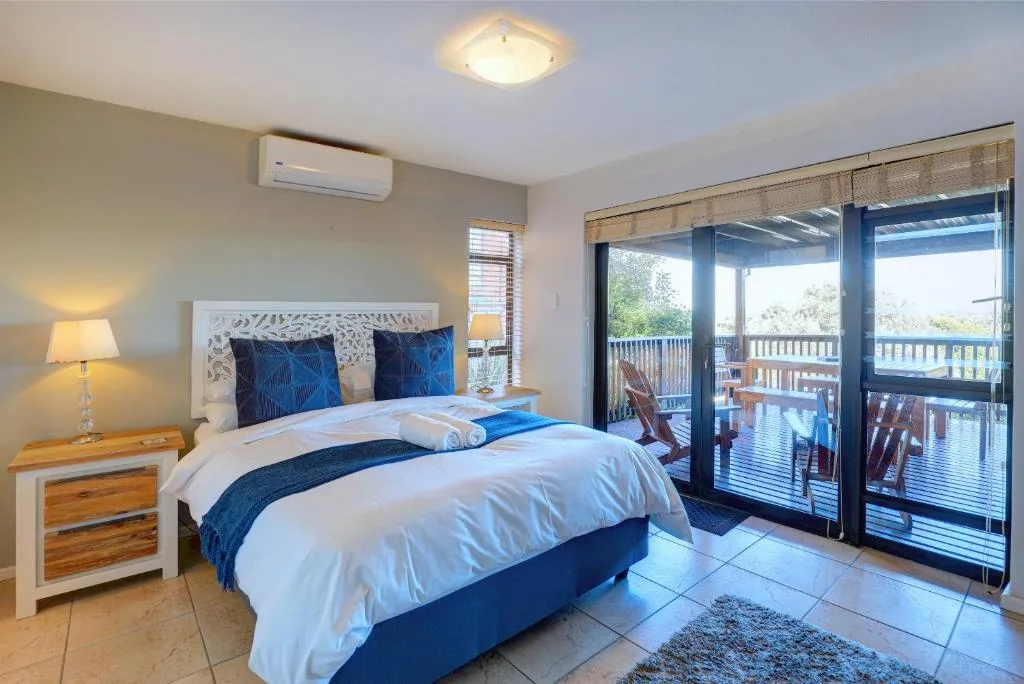 Bright bedroom with white bedding, blue accents, and sliding doors to deck