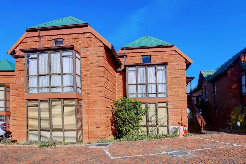 Red brick building with green roof and large windows, clear blue sky