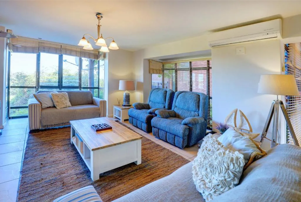 Spacious lounge with blue recliner, brown sofa, and large glass doors overlooking garden