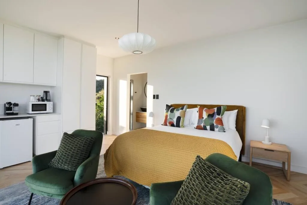 Modern bedroom with queen bed, yellow quilt, colorful pillows, and green armchairs