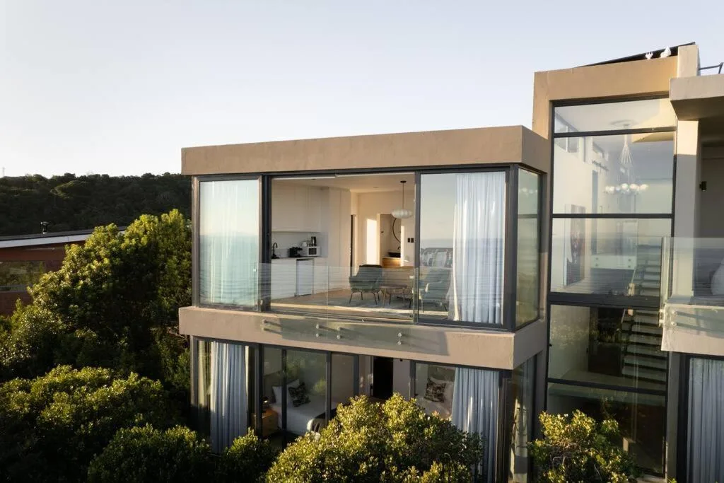 Modern beige apartment building with large glass windows and deck overlooking green landscape