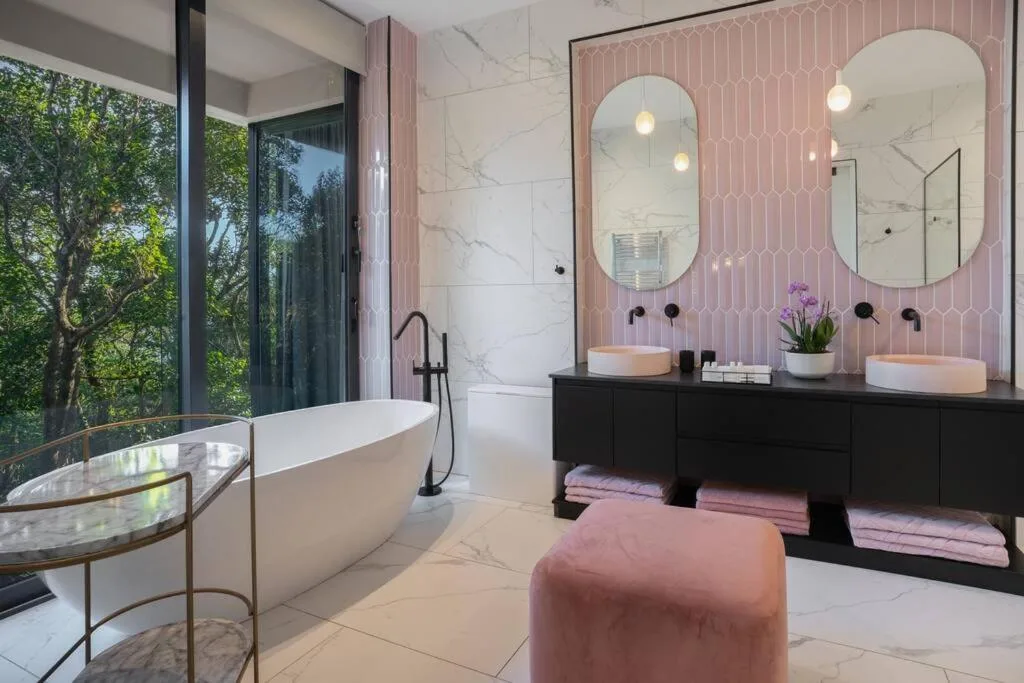 Modern bathroom with freestanding tub, dual vanity mirrors, and garden views
