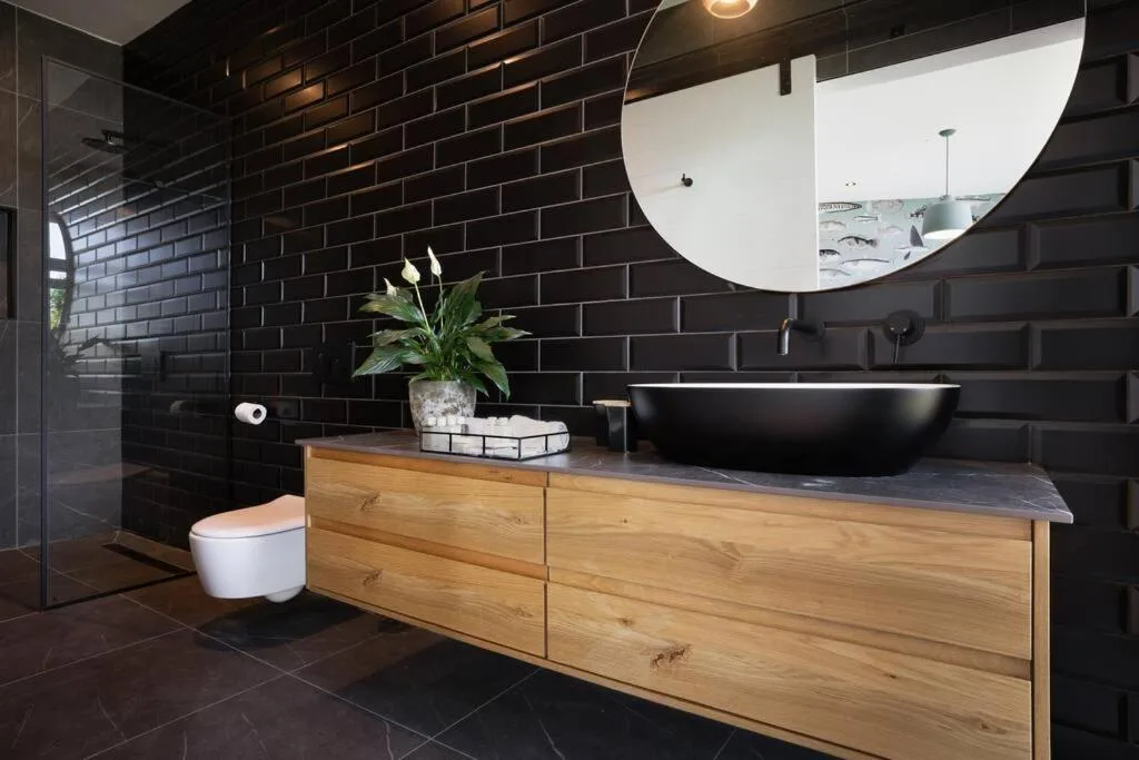 Modern bathroom with black brick walls, wooden vanity, and round mirror