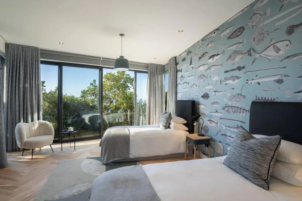 Modern bedroom with twin beds, fish-patterned wallpaper, and large windows overlooking garden