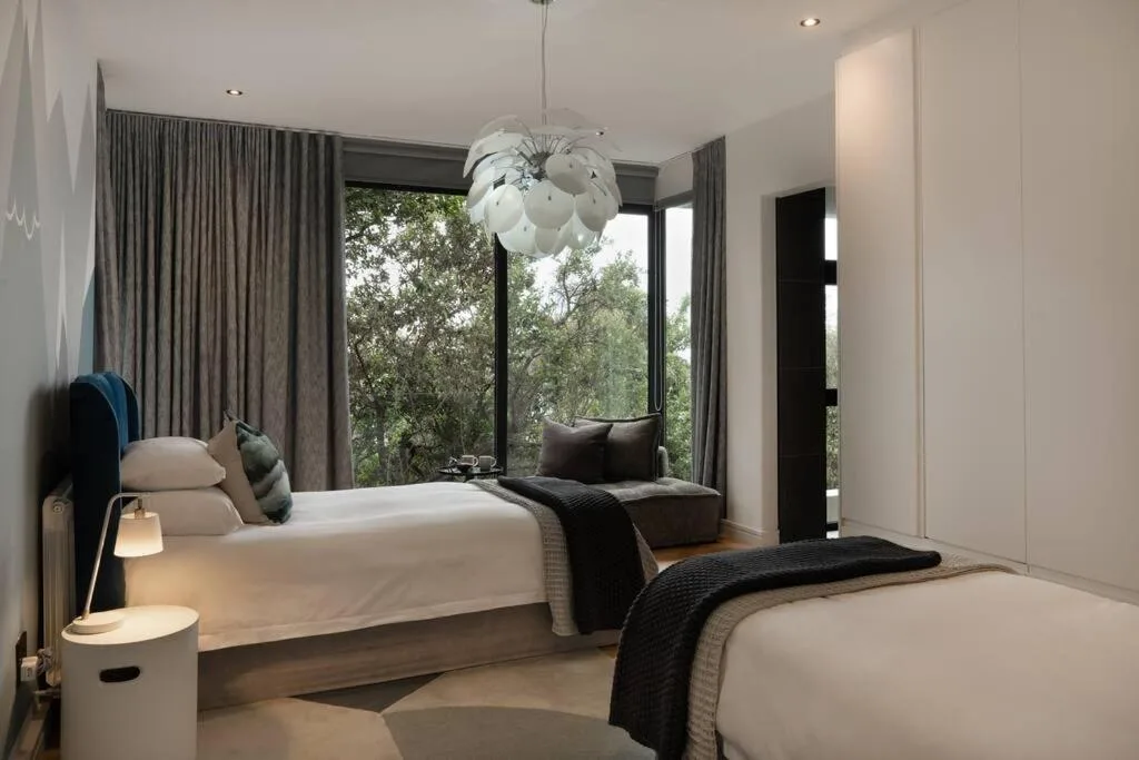 Modern bedroom with two beds, pendant light, and nature views through windows