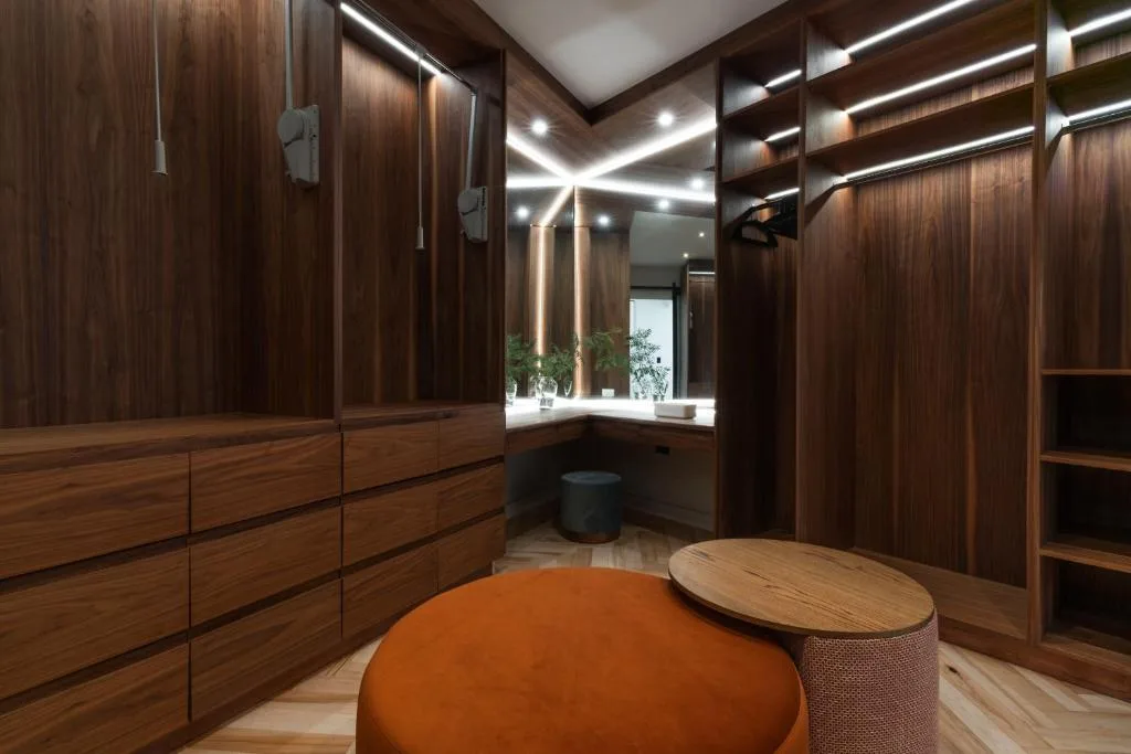 Luxury walk-in closet with dark wood cabinetry, illuminated mirror, and modern seating
