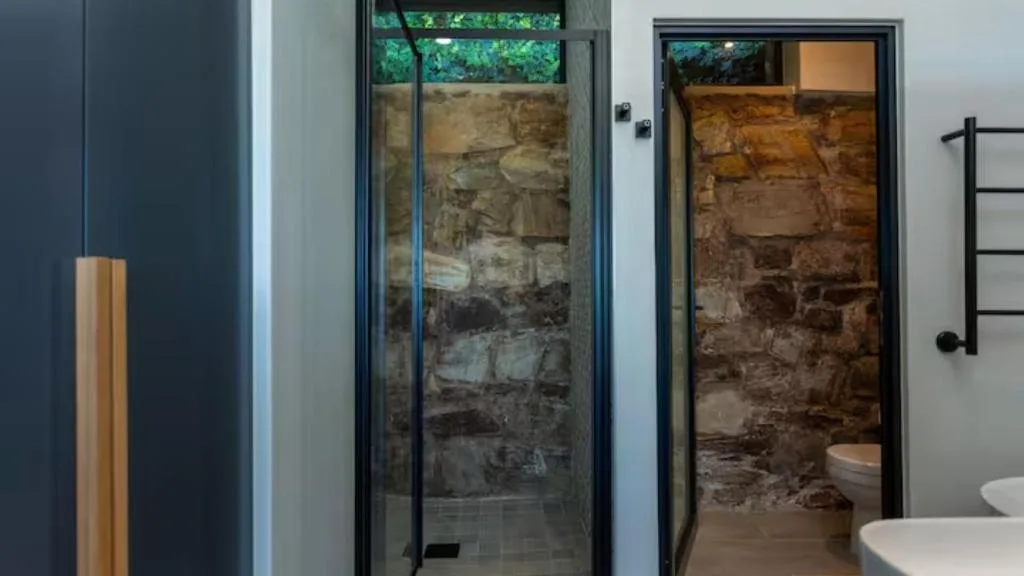 Modern bathroom with glass shower enclosure and rustic stone accent wall
