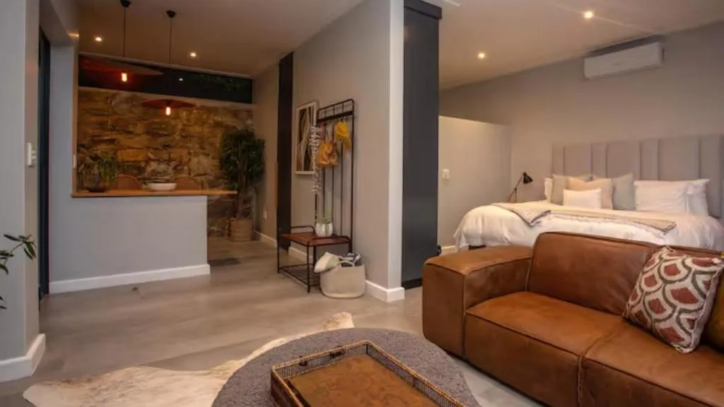 Modern bedroom with queen bed, leather sofa, and open-plan living area