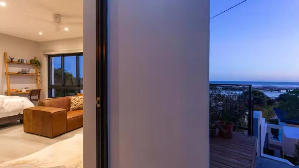 Modern bedroom with ocean views through glass doors and coastal landscape beyond