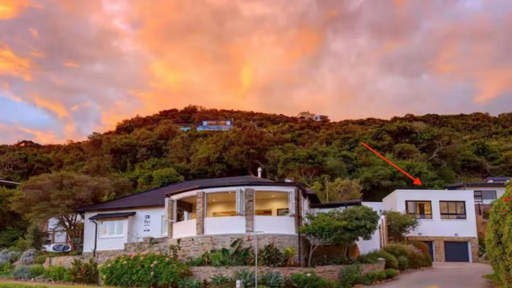 Modern white residential property on hillside at sunset with native vegetation