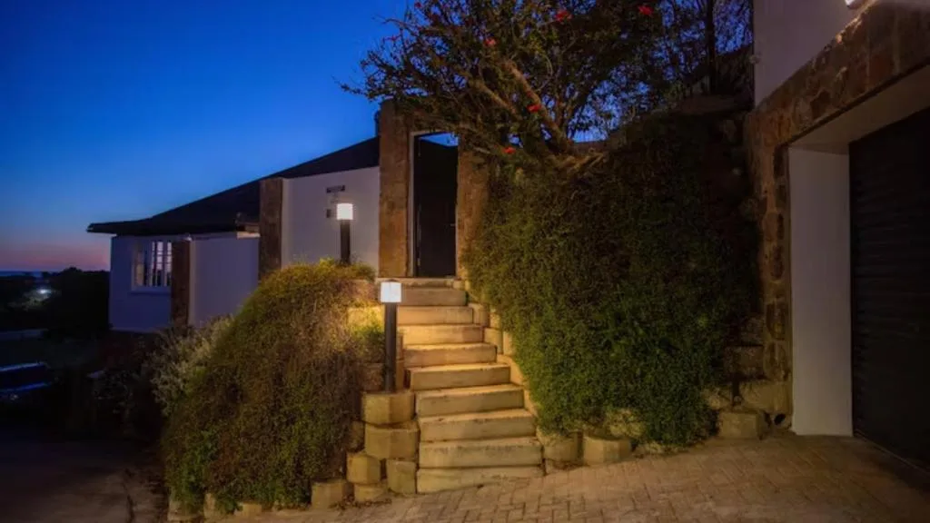 Modern apartment entrance at dusk with illuminated pathway and manicured hedges