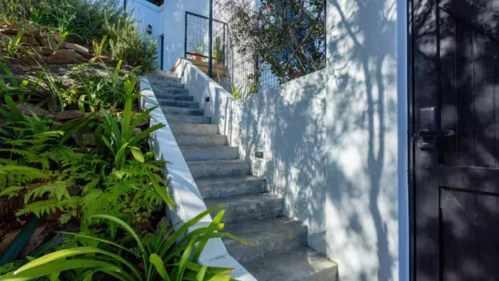 White staircase with blue trim leading up to property entrance surrounded by lush garden