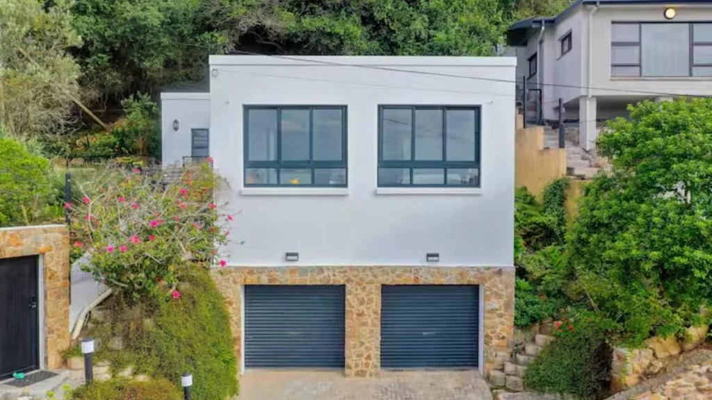 Modern white apartment building with stone base, double garage doors, and flowering plants