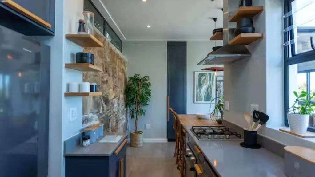 Modern kitchen with gas cooktop, stone feature wall, wooden shelves, and natural light