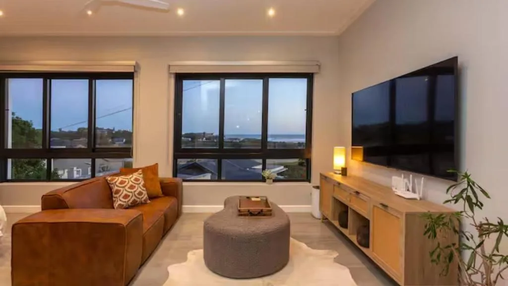 Modern lounge with orange sofa, TV, and ocean views through large windows