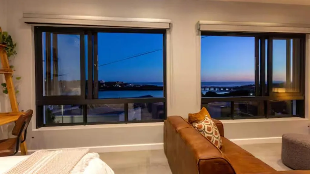 Modern lounge with cognac leather sofa overlooking blue lagoon at dusk